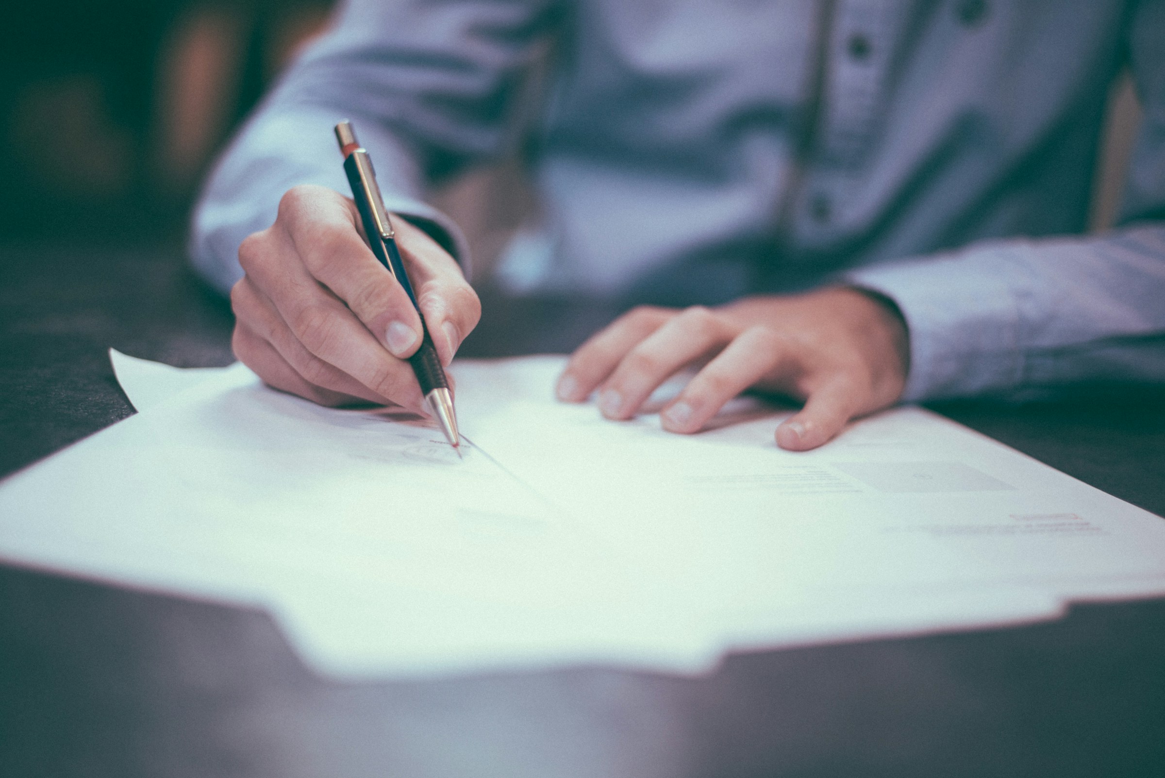 Person signing a document with a pen at a desk